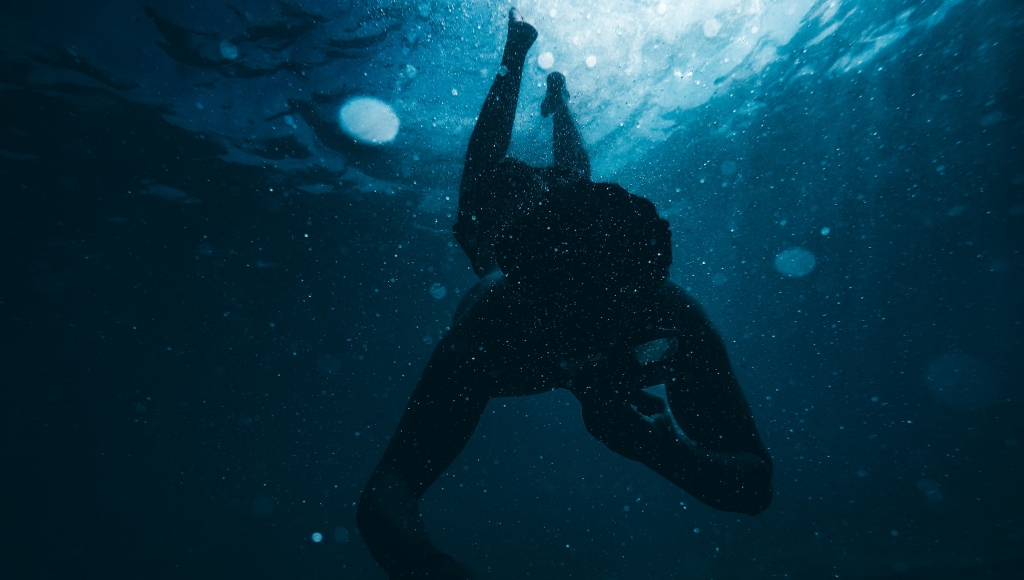 The silhouette of a person falling through open ocean with light filtering down from above.
