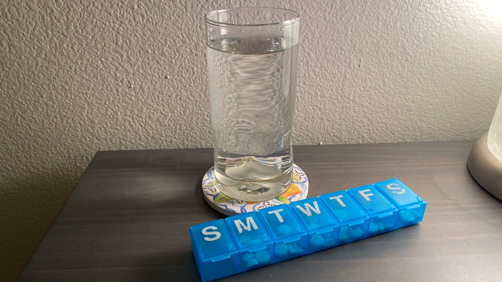 A blue seven-day pill organizer filled with medication near a glass of water on a coaster